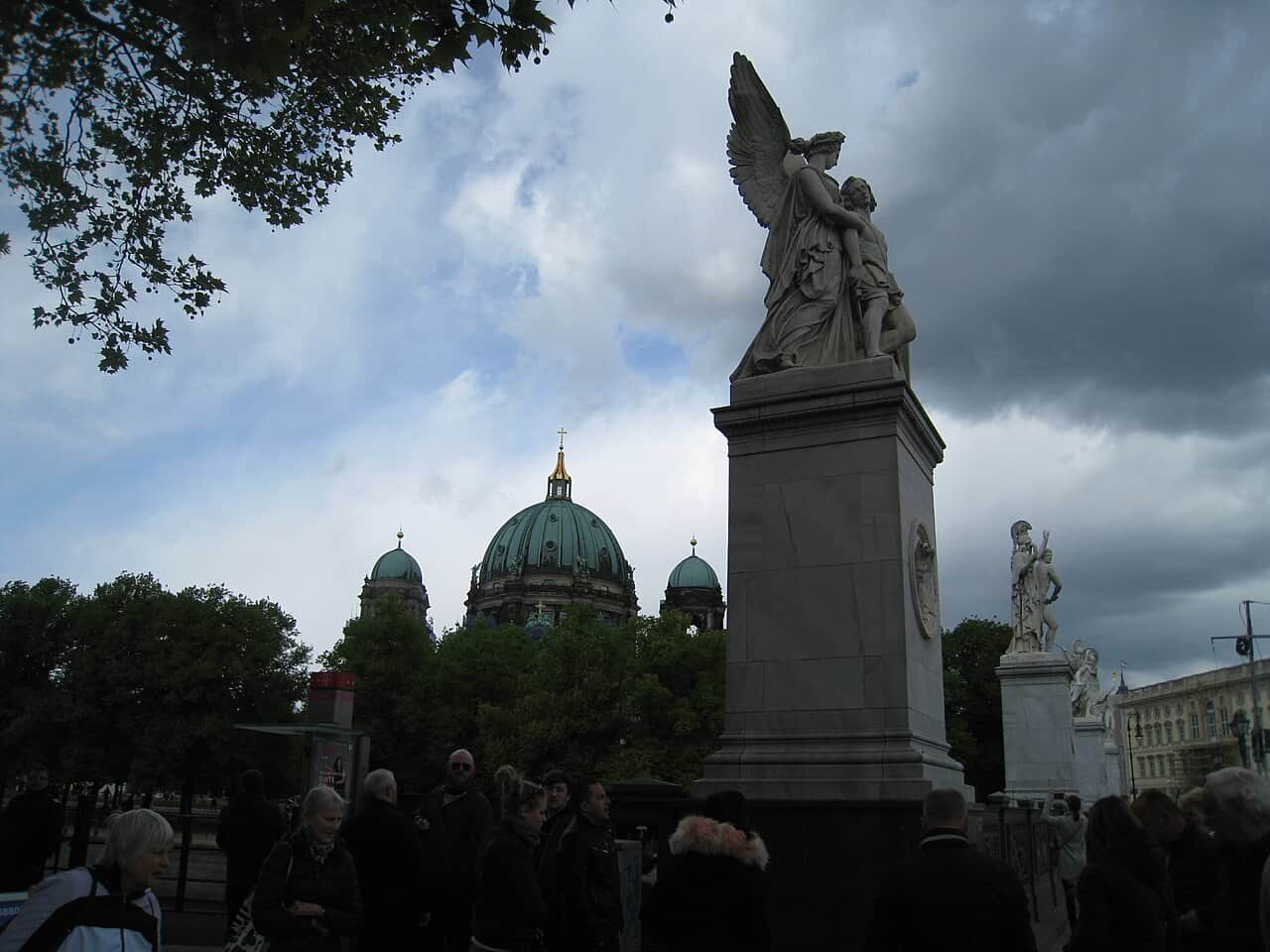 La cúpula verde de la catedral de Berlín tras una estatua de un ángel en el puente de la Isla de los Museos
