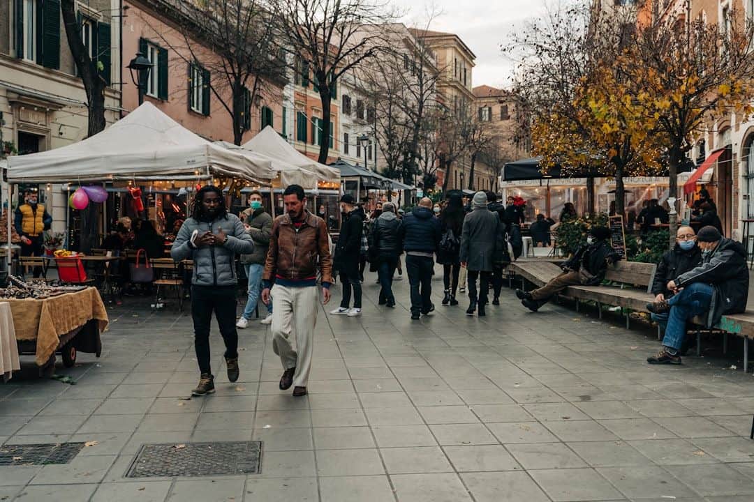 Persone che passano davanti a bancarelle e tavolini di un caffè in una strada di Roma